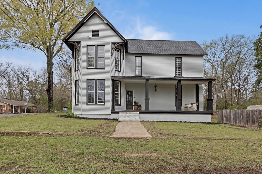 victorian house featuring a front lawn, fence, a shingled roof, and a porch