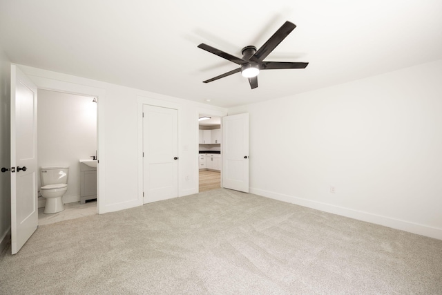 unfurnished bedroom with baseboards, a ceiling fan, connected bathroom, and light colored carpet