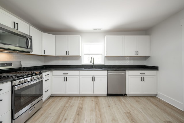 kitchen with white cabinets, a sink, light wood-type flooring, appliances with stainless steel finishes, and dark countertops