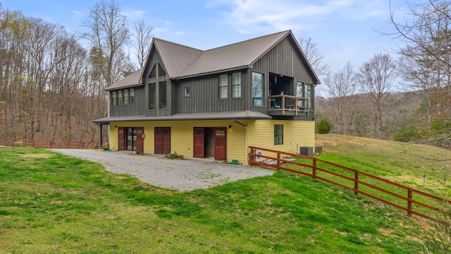 back of property with cooling unit, fence, metal roof, board and batten siding, and a yard