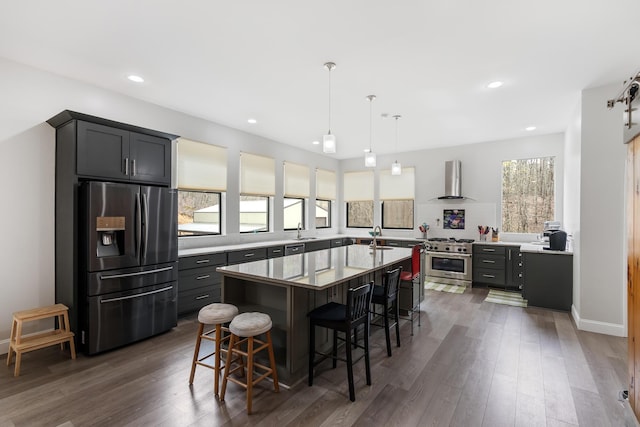 kitchen with wall chimney exhaust hood, stainless steel appliances, dark wood-type flooring, a breakfast bar area, and a center island