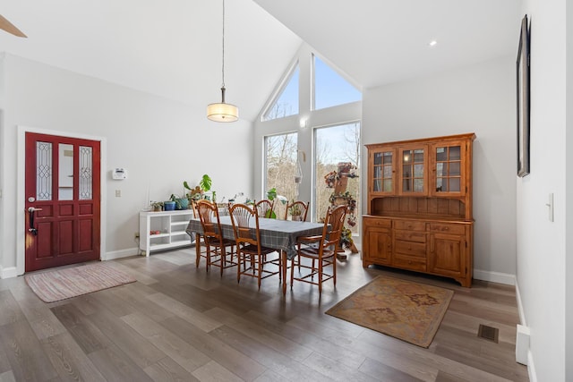 dining area featuring baseboards, high vaulted ceiling, and wood finished floors