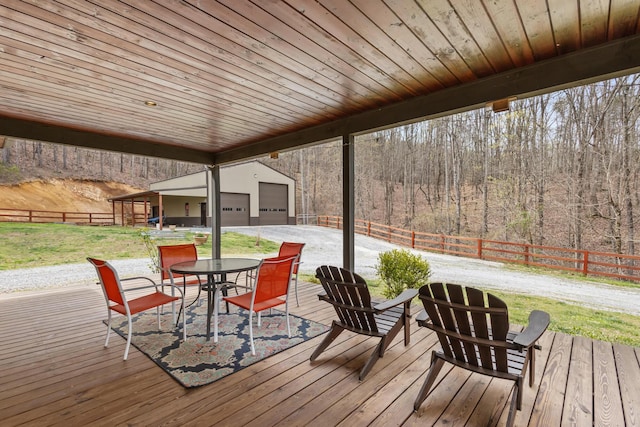 wooden terrace featuring outdoor dining area, a fenced backyard, a forest view, a lawn, and an outdoor structure
