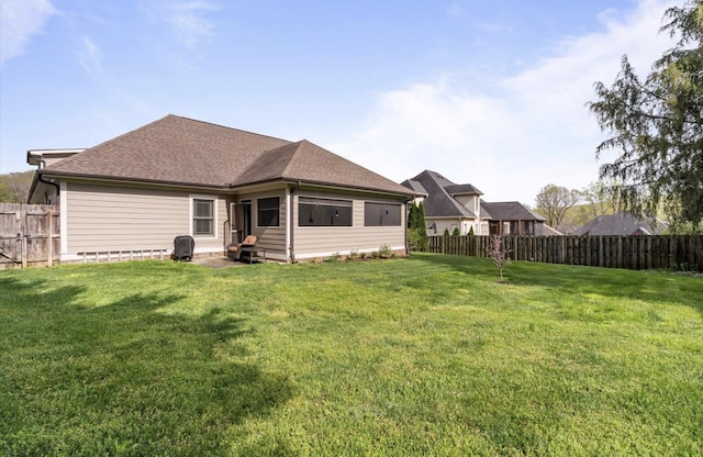 rear view of property featuring a fenced backyard, roof with shingles, and a yard