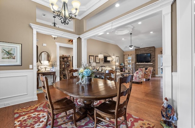 dining space featuring a wainscoted wall, wood finished floors, a decorative wall, ceiling fan with notable chandelier, and ornamental molding