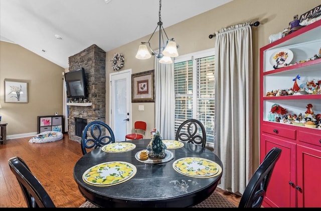 dining area with vaulted ceiling, an inviting chandelier, baseboards, a stone fireplace, and wood finished floors