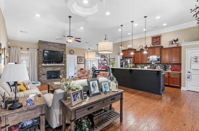 living area featuring crown molding, ceiling fan, visible vents, light wood-style flooring, and a fireplace