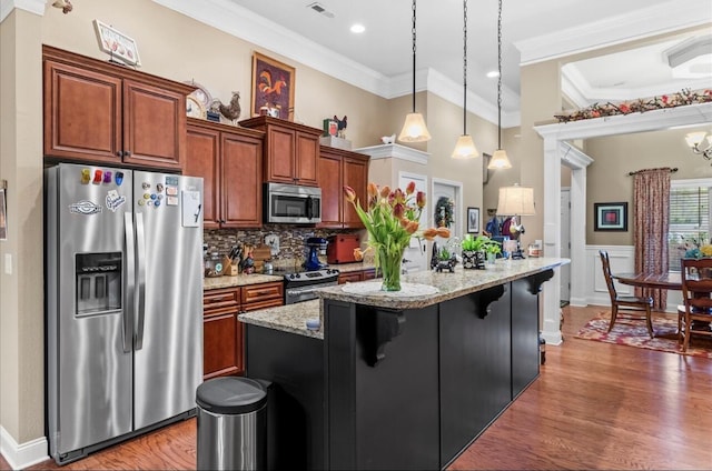 kitchen with decorative light fixtures, wood finished floors, a breakfast bar, and appliances with stainless steel finishes