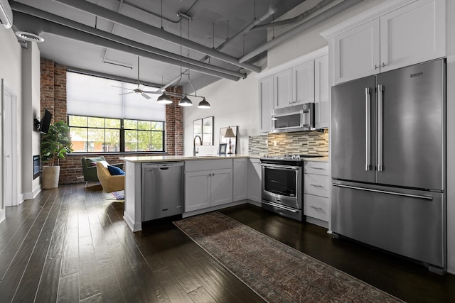 kitchen featuring dark wood-style flooring, stainless steel appliances, a sink, brick wall, and a peninsula