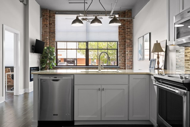 kitchen with dark wood-style flooring, a sink, stainless steel appliances, and brick wall