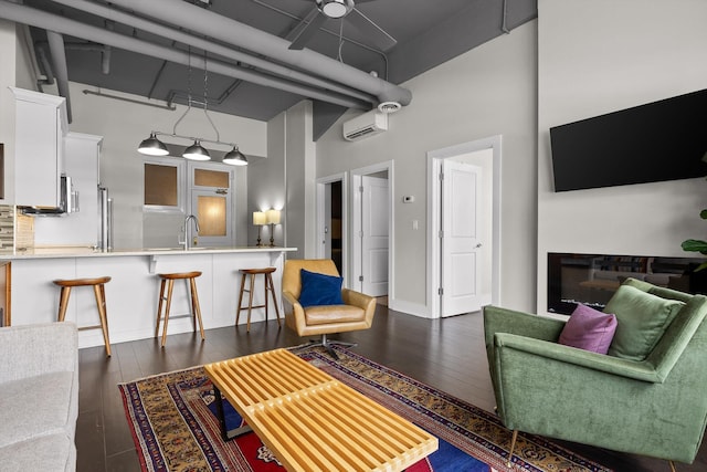 living area featuring a high ceiling, dark wood-style flooring, baseboards, and a wall mounted air conditioner