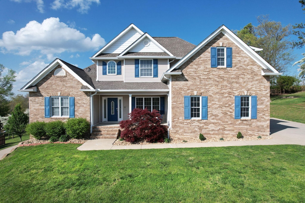 craftsman inspired home with brick siding, a front lawn, covered porch, and roof with shingles