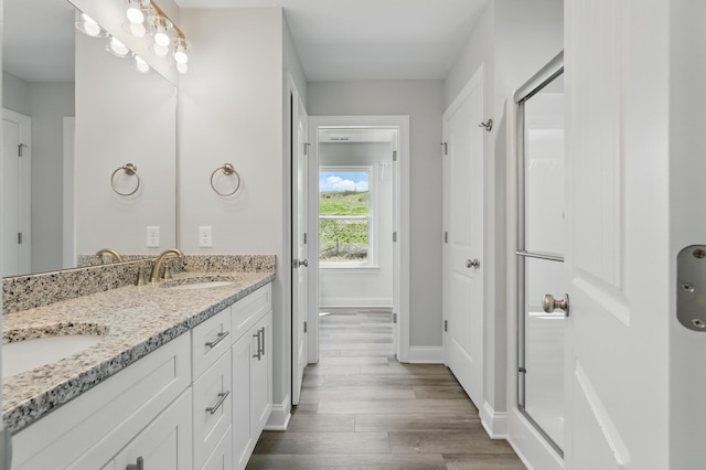 bathroom featuring double vanity, a sink, a stall shower, and wood finished floors