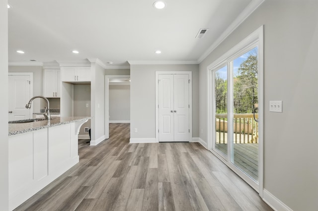 kitchen with white cabinets, light wood finished floors, baseboards, a sink, and light stone counters