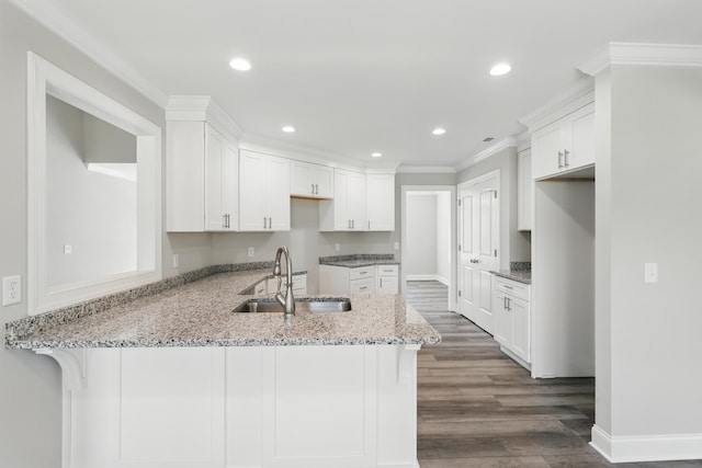 kitchen with crown molding, dark wood finished floors, a sink, light stone counters, and a peninsula