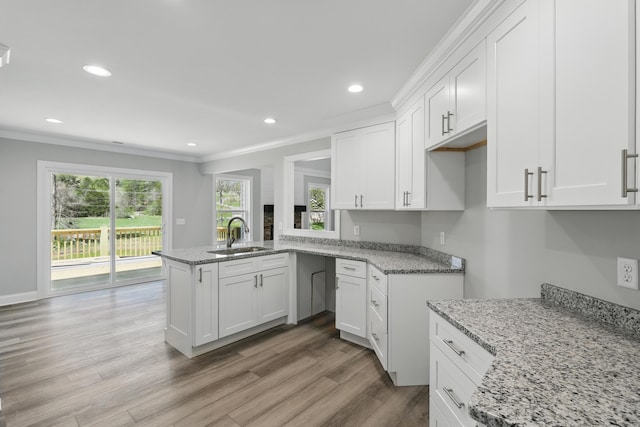 kitchen featuring white cabinets, ornamental molding, a sink, light wood-type flooring, and light stone counters