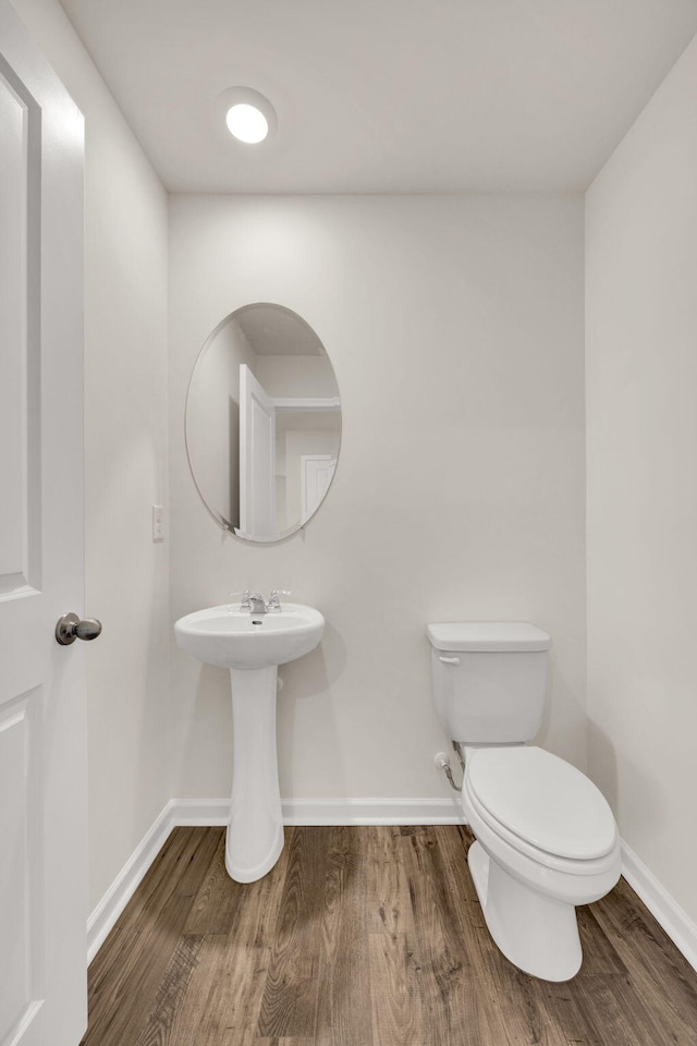half bath featuring toilet, baseboards, and wood finished floors