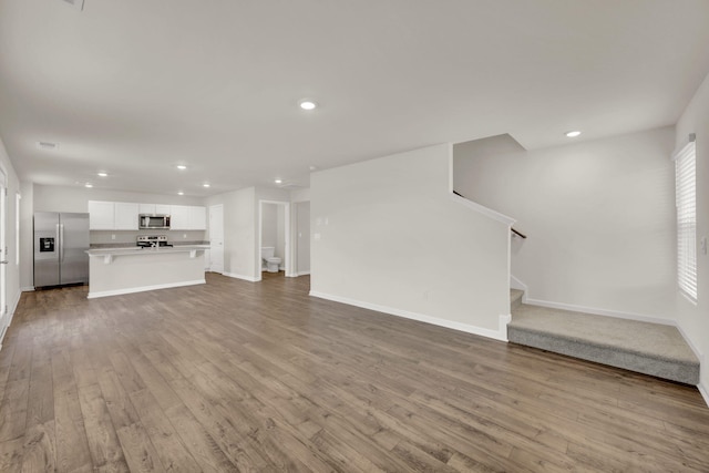 unfurnished living room with recessed lighting, baseboards, stairs, and wood finished floors