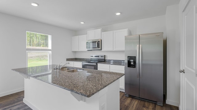 kitchen with white cabinets, stainless steel appliances, dark wood finished floors, a center island with sink, and a sink