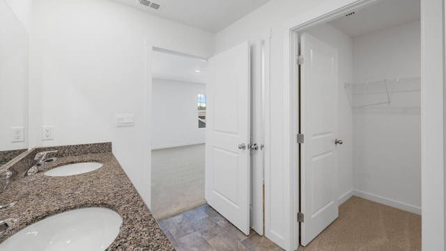 bathroom with visible vents, a walk in closet, a sink, and double vanity