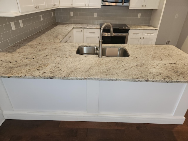 kitchen with decorative backsplash, stainless steel electric stove, a sink, light stone counters, and white cabinets