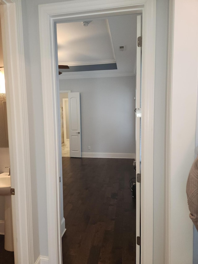 corridor featuring a raised ceiling, dark wood-style floors, crown molding, and baseboards
