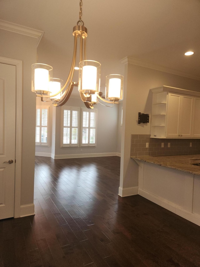 unfurnished dining area with an inviting chandelier, dark wood-style flooring, crown molding, and baseboards