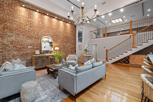 living room featuring light wood finished floors, visible vents, brick wall, a high ceiling, and stairs