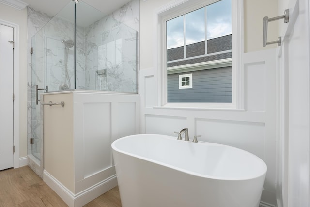 full bathroom featuring a freestanding bath, a decorative wall, a marble finish shower, and wood finished floors