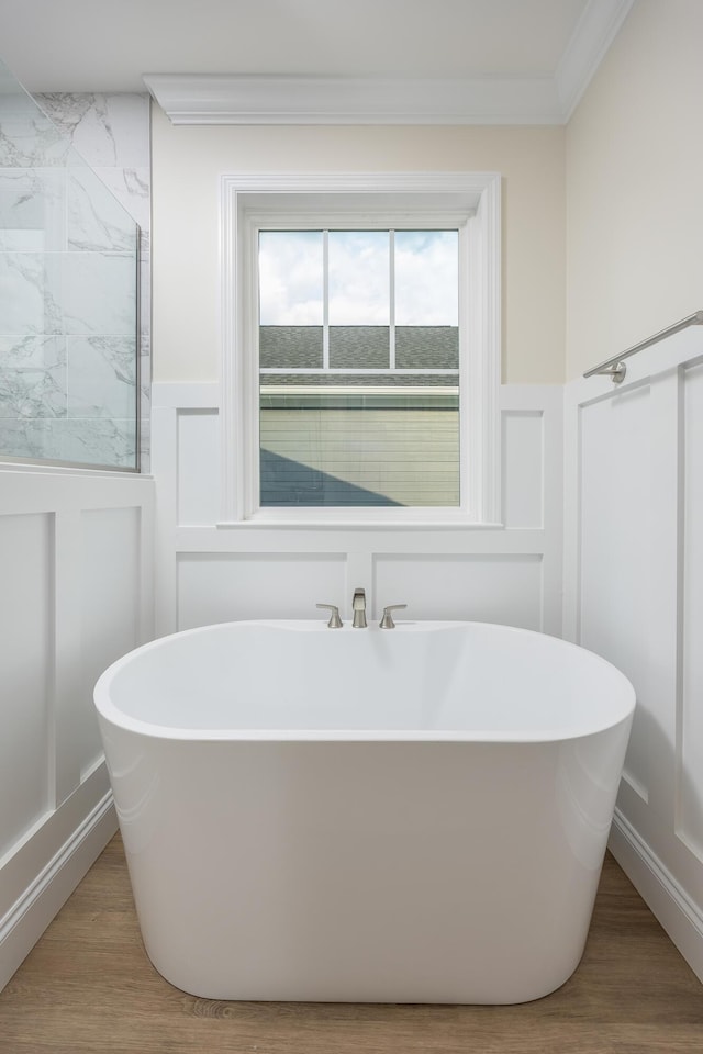 full bath featuring a decorative wall, a freestanding bath, wainscoting, and wood finished floors