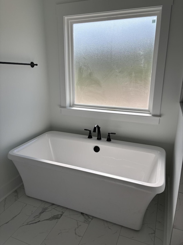 bathroom with a soaking tub, a healthy amount of sunlight, and marble finish floor