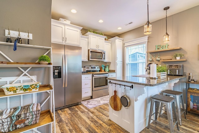kitchen featuring appliances with stainless steel finishes, wood finished floors, dark stone countertops, white cabinets, and a breakfast bar area