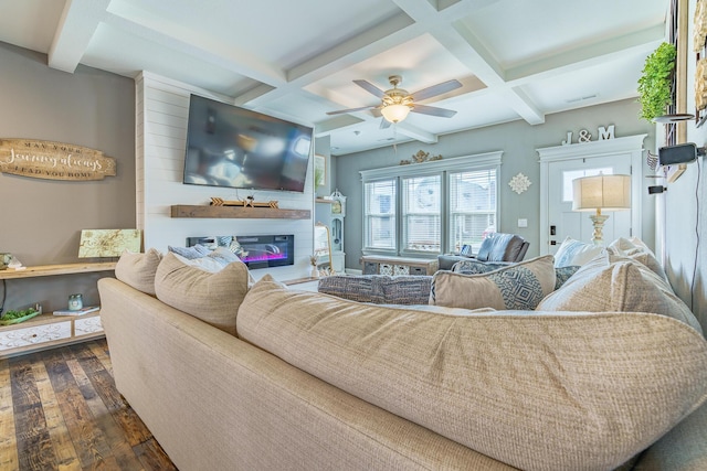 living area with coffered ceiling, dark wood-type flooring, beam ceiling, ceiling fan, and a glass covered fireplace