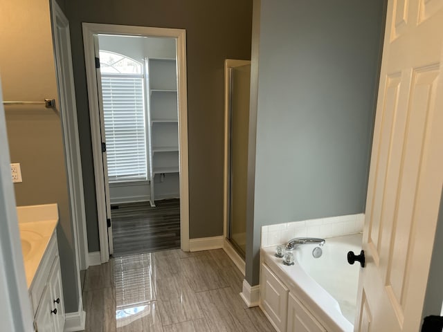 bathroom featuring baseboards, a shower stall, a garden tub, and vanity