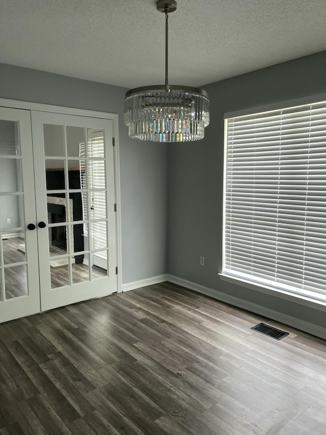 unfurnished dining area with visible vents, wood finished floors, a textured ceiling, french doors, and a notable chandelier