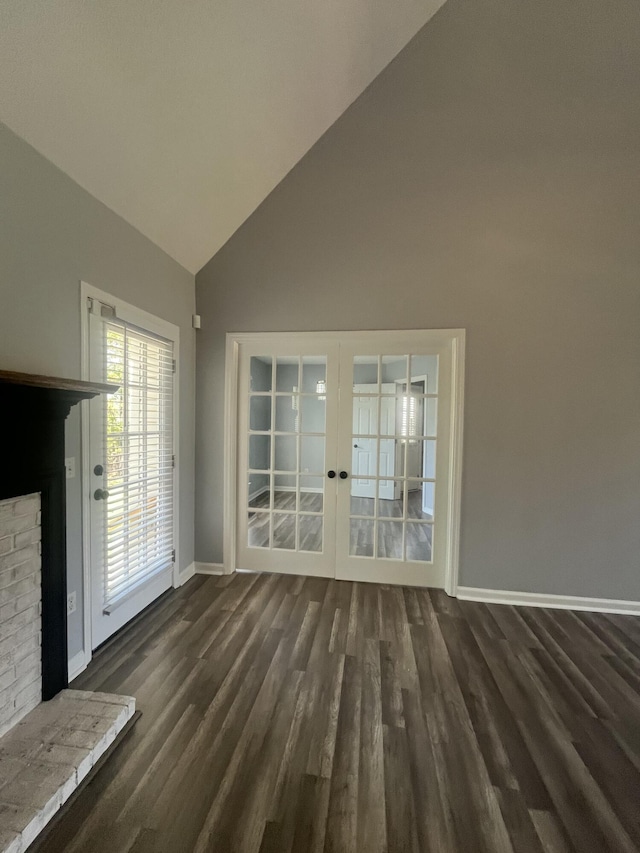 unfurnished living room featuring a brick fireplace, baseboards, high vaulted ceiling, dark wood-type flooring, and french doors