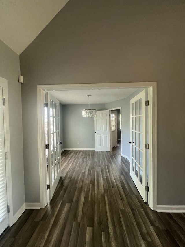 unfurnished dining area featuring baseboards, french doors, dark wood finished floors, and a chandelier