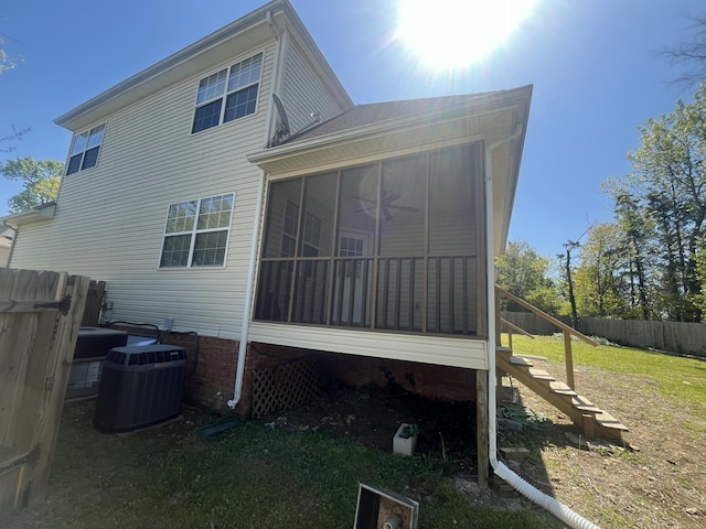 rear view of house with fence, a sunroom, stairway, central air condition unit, and a lawn