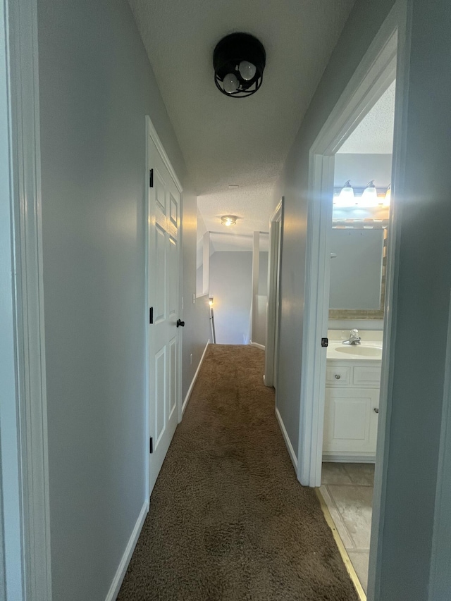 hallway with baseboards, light carpet, and a sink