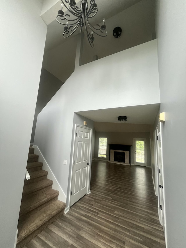 stairs featuring an inviting chandelier, a high ceiling, a fireplace, and wood finished floors