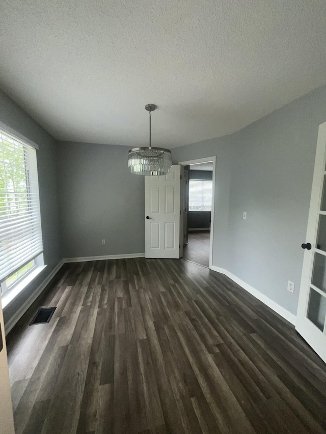 unfurnished dining area with an inviting chandelier, baseboards, dark wood-style flooring, and a textured ceiling