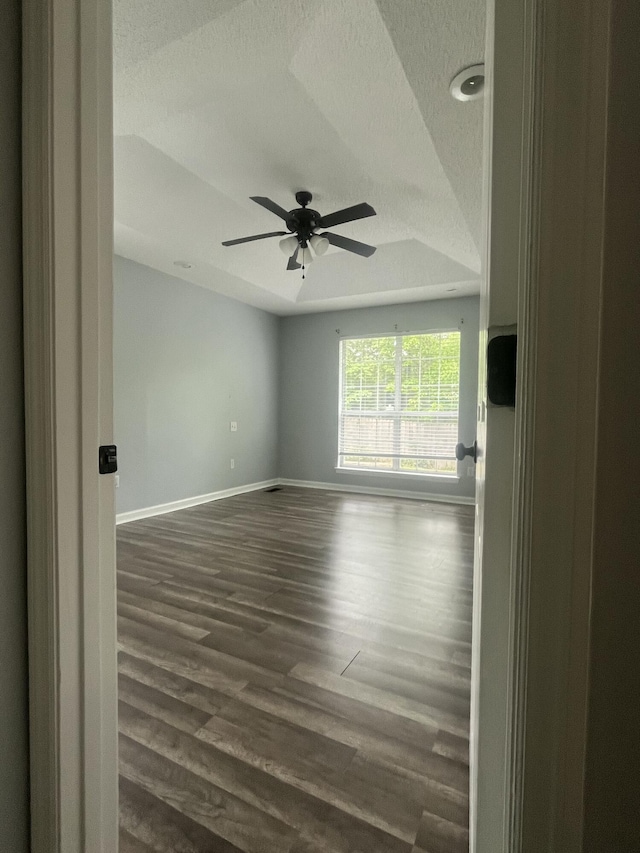 spare room with baseboards, a ceiling fan, a textured ceiling, and dark wood-type flooring