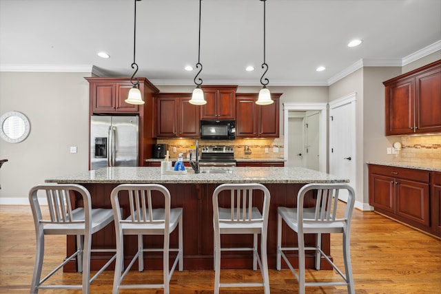 kitchen with an island with sink, crown molding, pendant lighting, light wood-type flooring, and stainless steel appliances