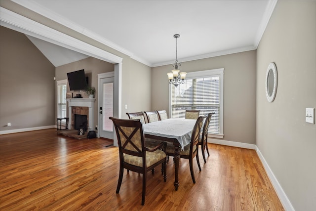 dining area featuring light wood-style flooring, crown molding, baseboards, a fireplace with raised hearth, and an inviting chandelier