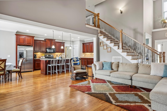living area with stairs, light wood-type flooring, visible vents, a towering ceiling, and recessed lighting