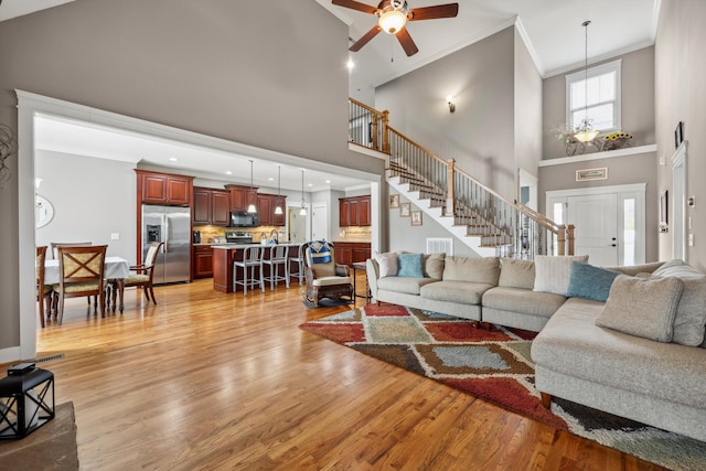 living area with stairs, crown molding, light wood-type flooring, and ceiling fan with notable chandelier