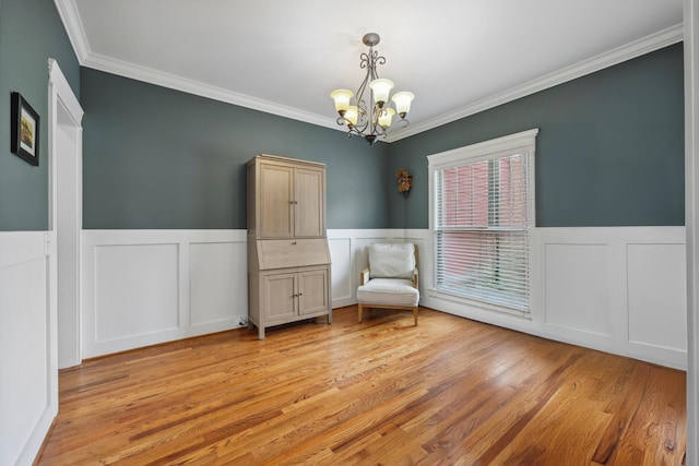 unfurnished room featuring wainscoting, crown molding, light wood-style flooring, and a chandelier