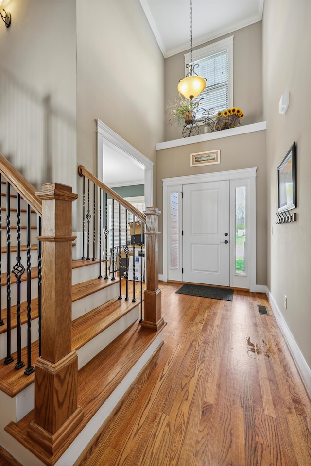entryway featuring baseboards, stairs, ornamental molding, wood finished floors, and a high ceiling