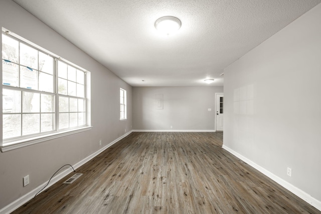 spare room featuring wood finished floors, a textured ceiling, baseboards, and visible vents