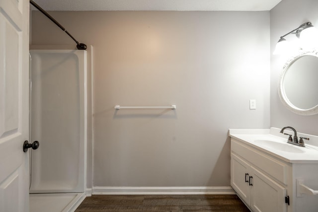 full bathroom with wood finished floors, vanity, baseboards, and a shower stall